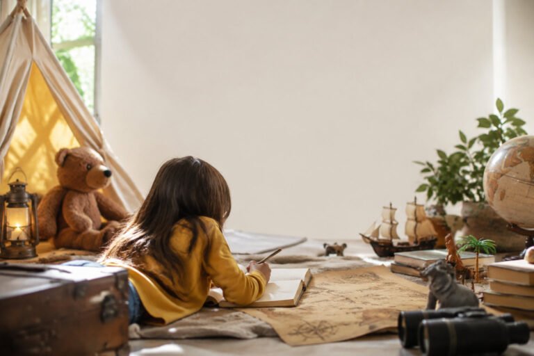 A young girl lying on the floor writing in a journal next to a play tent, globe, and vintage map.